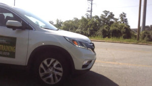 The front end of the drivers education car as a student drives down the road.